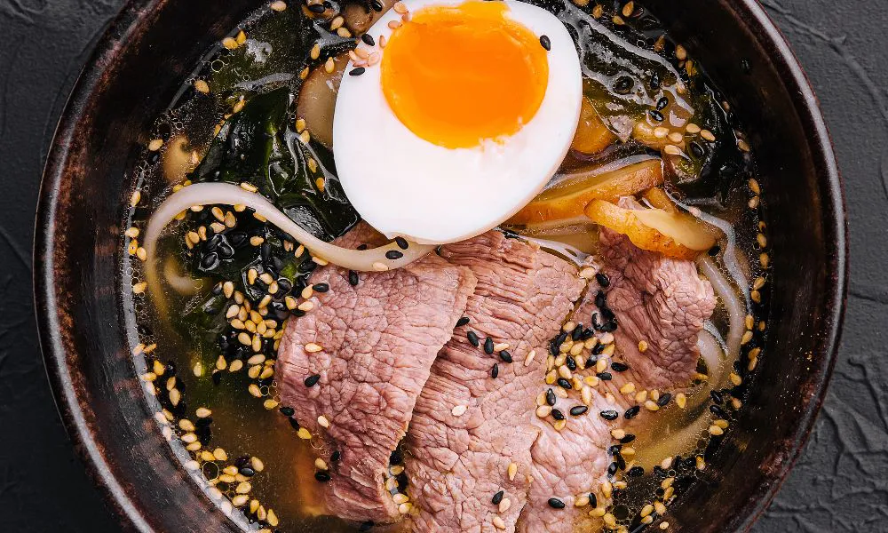 Bowl of beef ramen soup with tender sliced beef, runny-yolk soft boiled egg, seaweed, bamboo shoots and sprinkled black and white sesame seeds